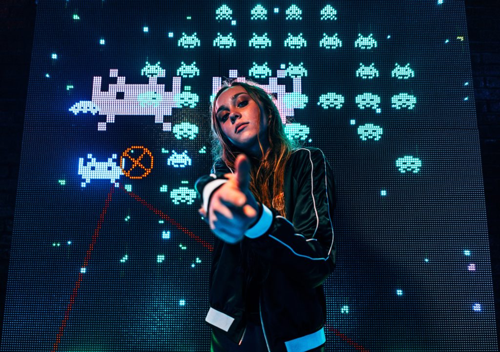 Une jeune joueuse pointant sa main façon pistolet avec les ennemis du jeu Space Invaders derrière elle