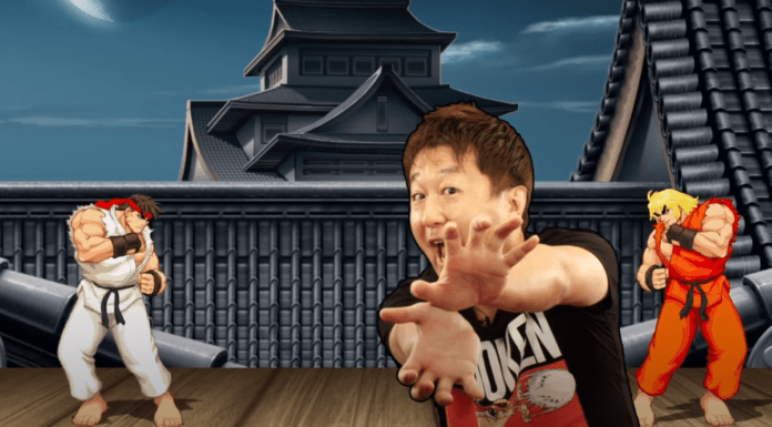 Yoshinori Ono de chez Capcom qui mime un hadoken avec les mains jointes devant une partie de street Fighter II