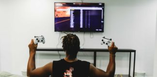 Un homme noir tenant deux manettes de Xbox devant la télé