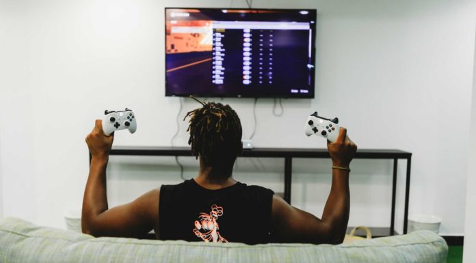 Un homme noir tenant deux manettes de Xbox devant la télé